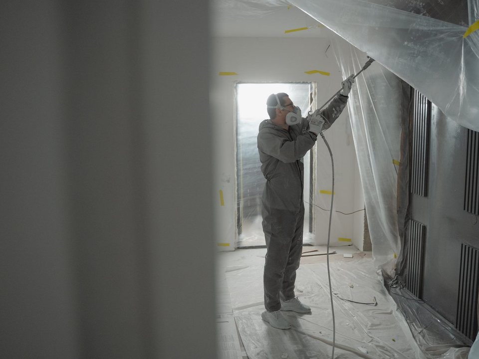 Sanierer in Vollschutz arbeitet in einem folienverkleideten Raum